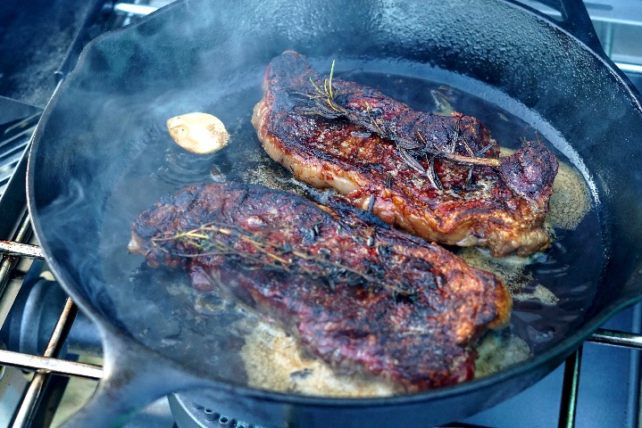 New York strip steaks searing in cast iron skillet.