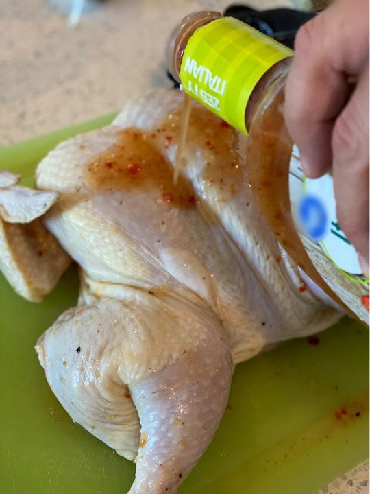 Prepping the zesty grilled spatchcock chicken by applying some zesty Italian dressing.