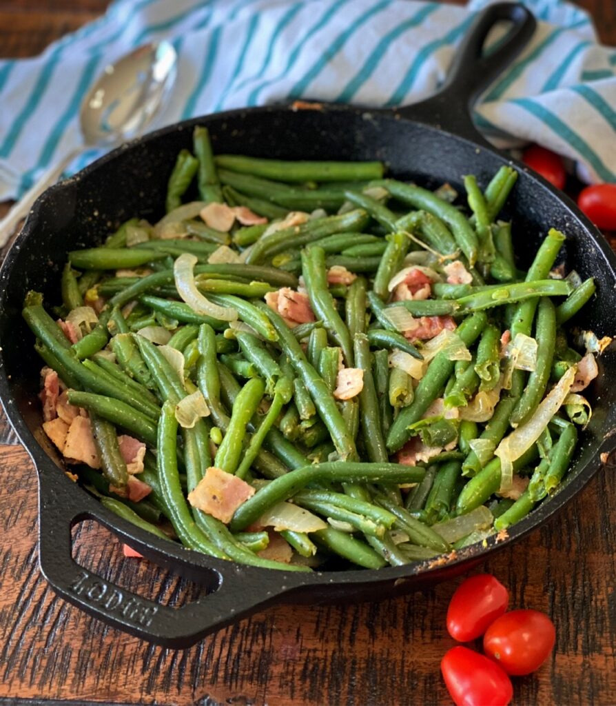 Green beans with bacon and onion in a cast iron skillet on a table.