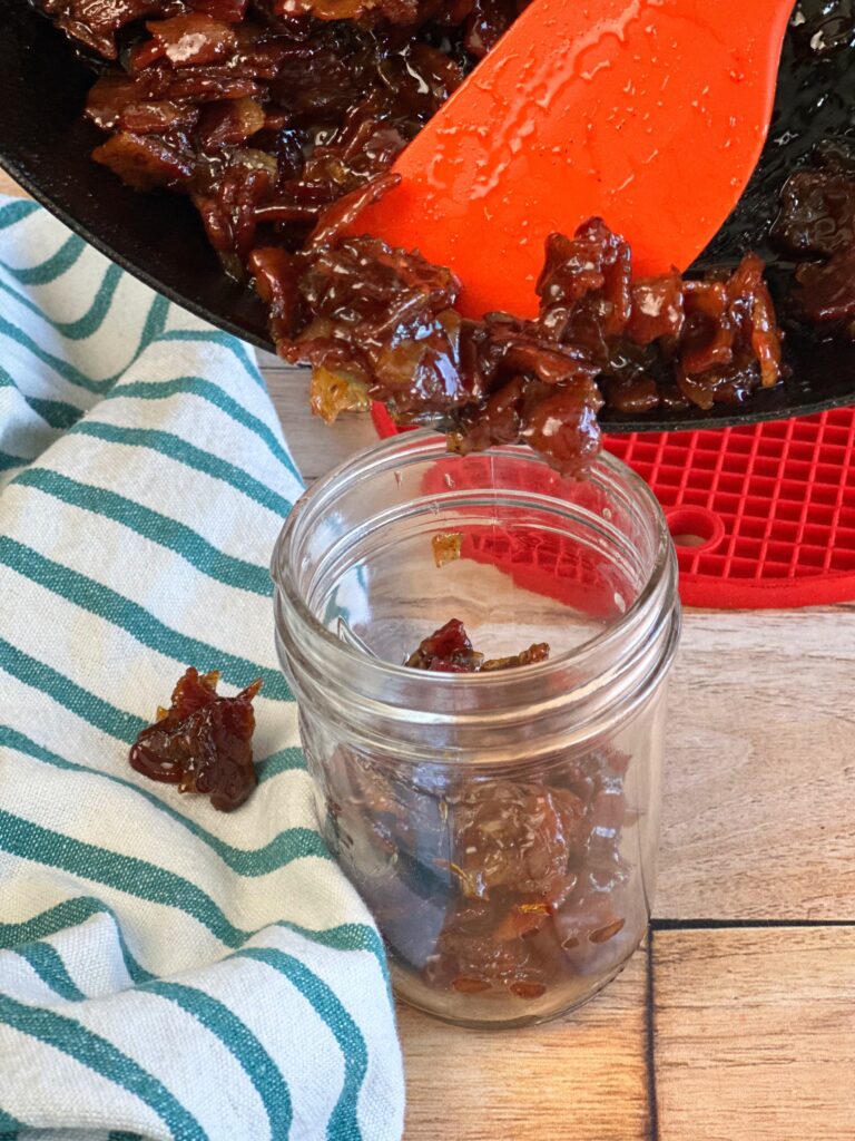 Bacon jam being scooped into a jar for later usage.